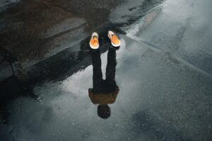 orange shoes on a wet sidewalk. in the watery reflection, a person can be seen below the shoes, Some kind of reverse vampire maybe? Or just a really cool photoshop trick.