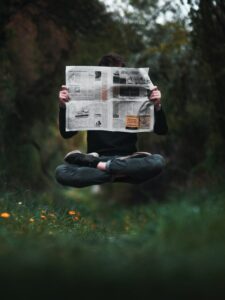 a man floating above a field in a sitting position and reading a newspaper. A common thing to see among the floating population. They love to keep up with current events.