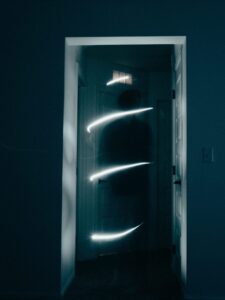 a shadowy figure appearing in a doorway with four bands of bright light surrounding her.