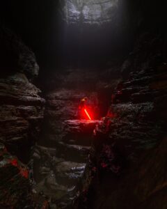 A sith lord standing with a red lightsaber in a dark cave.