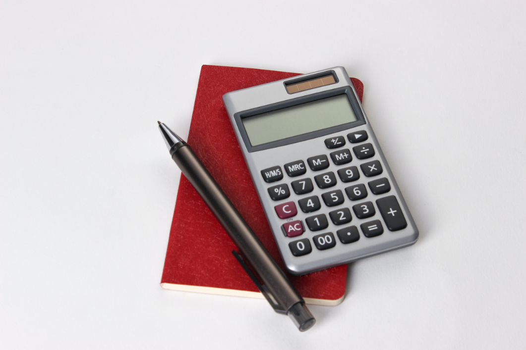 A calculator and pen atop a small red notebook.